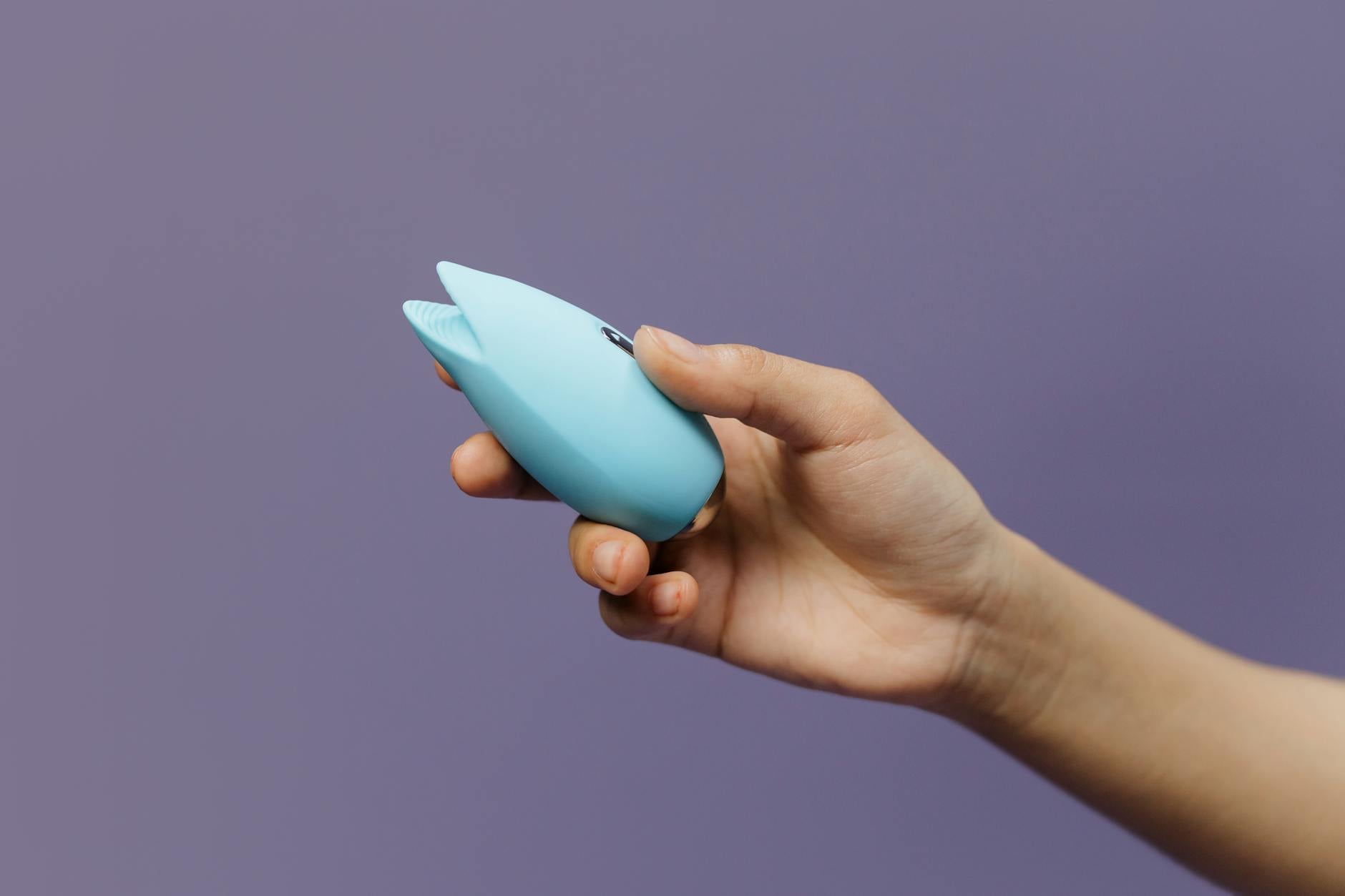 A blue silicone clitoral vibrator held in hand, designed for sensitive tissue and gentle stimulation